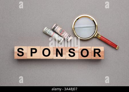 Word Sponsor realizzato in cubi di legno con lettere, banconote in dollari e lente d'ingrandimento su tavolo grigio, vista dall'alto Foto Stock