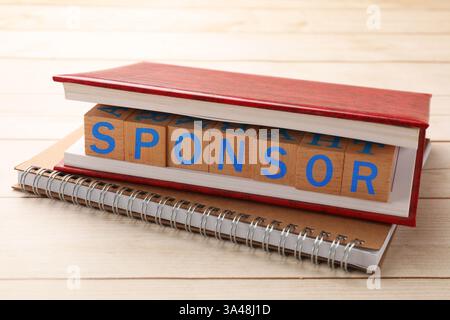 Word Sponsor in cubi di legno con lettere tra le pagine del quaderno su un tavolo di legno Foto Stock