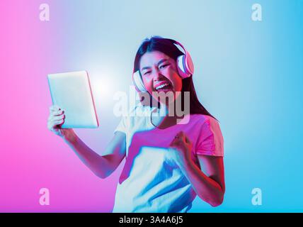Una giovane donna ascolta la musica con le cuffie mentre tiene in mano un tablet Foto Stock