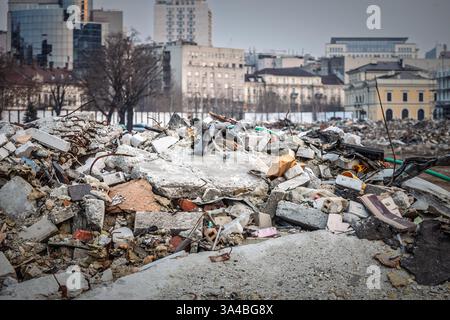 Mucchio di detriti di costruzione tra cui cemento, mattoni e metallo ritorto da un edificio demolito, con il paesaggio urbano di Belgrado sullo sfondo. Foto Stock