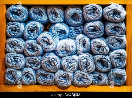 File di palle in filato blu ben organizzate riempiono uno scaffale in legno, mostrando varie sfumature e texture per la lavorazione. Foto Stock