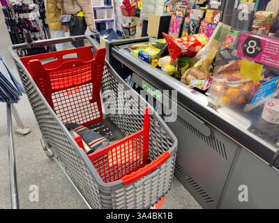 Parigi, Francia - 23 dicembre 2024: Carrello alla cassa pieno di generi alimentari assortiti, tra cui prodotti freschi, spuntini confezionati, prodotti in scatola e mag Foto Stock