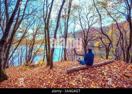 Un solo uomo seduto su un tronco sulla riva del lago di montagna in autunno Foto Stock