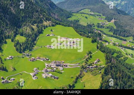 Vista aerea panoramica dell'idilliaco villaggio alpino circondato da lussureggianti colline verdi vicino alla Valle di Funes alle Dolomiti, Italia Foto Stock