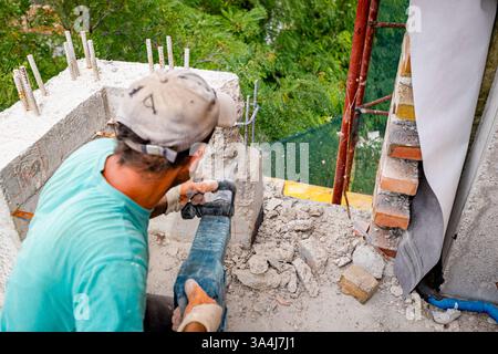 L'operaio edile sta utilizzando un martello elettrico per riallineare il cemento armato, rimuovendo, distruggendo e distruggendo l'eccesso sul recinto del balcone dell'edificio residenziale Foto Stock