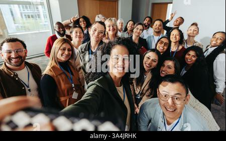 Diversi colleghi si riuniscono per scattare un divertente selfie, mostrando lavoro di squadra e cameratismo in un ambiente professionale. Foto Stock