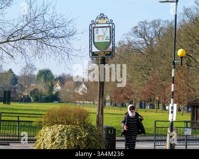 Cartello del villaggio di Theydon Bois, Essex, Regno Unito, con pedonale e verde villaggio sullo sfondo Foto Stock