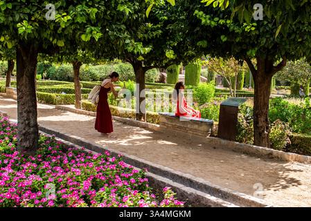 Due giovani donne attraenti che indossano abiti eleganti e colorati sono viste tra splendidi fiori e alberi in un giardino a Cordova in Spagna. Foto Stock