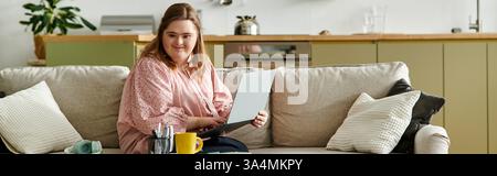 In una casa accogliente, una giovane donna sicura di sé con la sindrome di Down si impegna con il suo laptop. Foto Stock