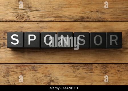 Word Sponsor realizzato in cubi neri con lettere su sfondo in legno, vista dall'alto Foto Stock