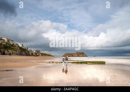 Coppia che cammina con i cani a Castle Beach, Tenby, Galles del Sud, Regno Unito. Foto Stock