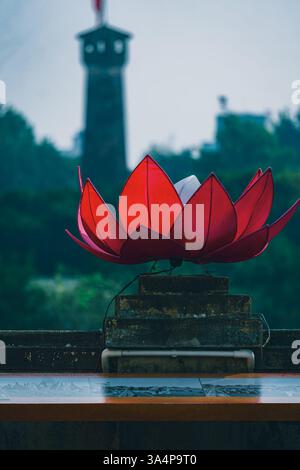 Primo piano di una luce decorativa di fiori di loto con sullo sfondo la Torre della bandiera di Hanoi. Foto scattata dall'interno della cittadella imperiale di thang Long. Foto Stock