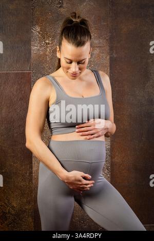 Donna incinta che tiene la pancia e pratica yoga su uno sfondo scuro Foto Stock