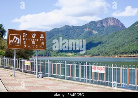 Contea di Damyang, Corea del Sud - 23 settembre 2020: Un cartello stradale marrone segna l'ingresso al lago Damyang, con le acque calme del bacino idrico riflesso Foto Stock