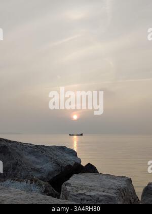 Una tranquilla alba/tramonto sul mare calmo, vista dalla costa rocciosa mentre una nave solitaria passa in lontananza a Pirano, in Slovenia. Foto Stock