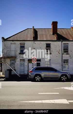 Una tranquilla scena di strada a Hobart, Tasmania: Muro di mattoni bianchi, SUV parcheggiato, segnale rosso di velocità sotto un cielo azzurro e cristallino, che incarna la calma urbana. Foto Stock