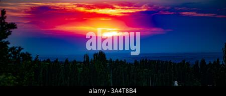 La fotografia cattura un pittoresco tramonto su un paesaggio collinare coperto da fitti alberi. Il sole sta tramontando dietro l'orizzonte, dipingendo il cielo Foto Stock