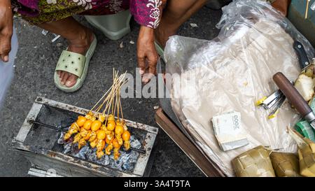 Venditore di strada che grigia il satay di pollo su una piccola griglia a carbone a yogyakarta, indonesia, riempiendo l'aria con deliziosi aromi e fumo Foto Stock
