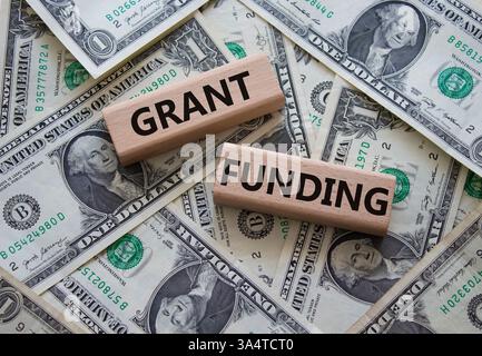 Simbolo di finanziamento della sovvenzione. Blocchi di legno con parole Grant funding. Bellissimo sfondo di dollari. Business e Grant funding. Copia spazio. Foto Stock
