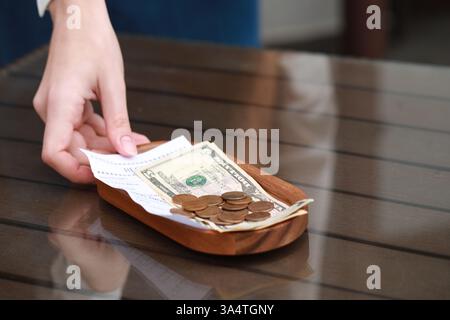 Cameriera che si prende mance e paga per l'ordine dal tavolo di legno nel caffè, primo piano. Spazio per il testo Foto Stock