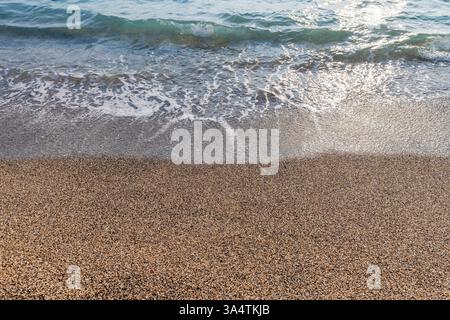 Tranquillo paesaggio costiero che presenta una spiaggia tranquilla ricoperta di ciottoli e dolci onde dell'oceano sotto la calda luce del sole, catturando la calma e la tranquillità Foto Stock