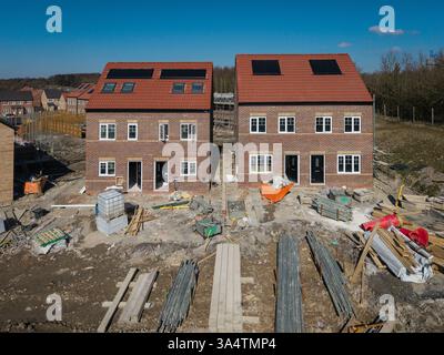 Una fila di case di nuova costruzione senza caratteristiche in un cantiere con pannelli solari integrati sul tetto per un'energia sostenibile e conveniente da utilizzare Foto Stock