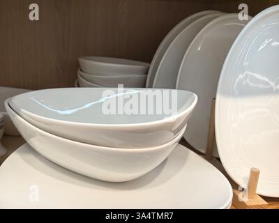 I piatti bianchi sovrapposti mostrano il loro design elegante in una cucina ben illuminata. La disposizione minimalista mette in risalto la raffinata maestria artigianale e la bellezza della sim Foto Stock