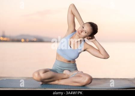Giovane e felice insegnante di fitness con esperienza esegue yoga parshvottanasana seduta sulla spiaggia al mattino Foto Stock