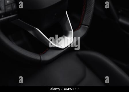 Parte inferiore del volante dell'auto con elementi argentati. Volante in pelle con cuciture rosse. Interni di un'auto moderna con sedili in pelle. Foto Stock