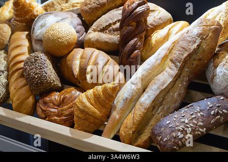 Un bancone da forno con una vasta gamma di panini, panini e baguette. Un'illuminazione calda e luminosa mette in risalto la freschezza. Foto Stock