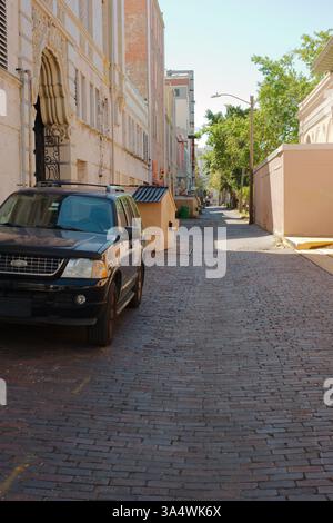 SUV parcheggiato in una strada di mattoni in un vicolo. Il veicolo si trova sul lato sinistro. Il vicolo è stretto e pavimentato con mattoni rossastro-marroni, che mostrano segni di Foto Stock