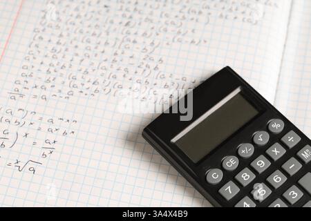 Copybook con formule matematiche scritte a mano e calcolatrice come sfondo, primo piano Foto Stock