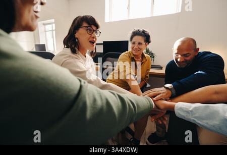 Un team è impegnato in una discussione collaborativa, mostrando unità ed entusiasmo unendo le mani. L'immagine riflette un ambiente di lavoro professionale Foto Stock