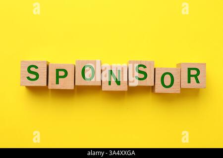 Word Sponsor in cubi di legno con lettere su sfondo giallo, vista dall'alto Foto Stock