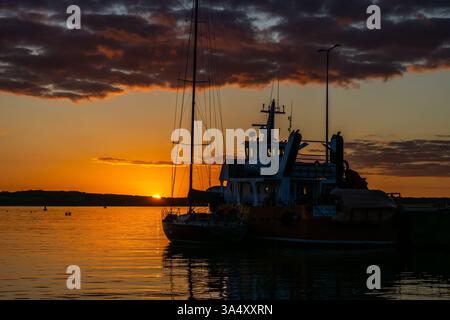 Baltimora, West Cork, Irlanda. 15 marzo 2025. Dopo una giornata di sole caldo, il sole tramonta sul porto di Baltimora con il traghetto Cape Clear "Dún an Óir II" Foto Stock