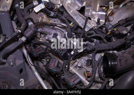 Vano motore parzialmente smontato di una vettura con il coperchio motore rimosso, le candele rimosse e il cablaggio esposto Foto Stock
