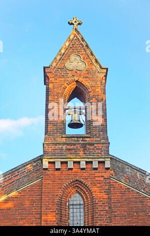 Primo piano della torre della chiesa in mattoni rossi e dell'apice con campana a vista singola nell'alloggiamento sormontato da una croce a Loves Green Highwood Essex Inghilterra Regno Unito Foto Stock