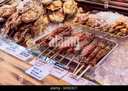 Una selezione di pesce fresco, tra cui gamberi tigre spiedati calamari e capesante, è organizzata su ghiaccio tritato in un mercato del pesce di Tokyo a prezzi scritti a mano Foto Stock
