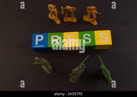I blocchi colorati scrivono la stampa con soldati in miniatura che rappresentano notizie e temi mediatici su uno sfondo scuro. Foto Stock