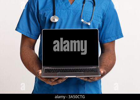 Primo piano delle mani di un medico afroamericano che presenta uno schermo vuoto per laptop su uno sfondo bianco. Lo spazio di copia lo rende ideale per i mockup di siti Web medici, il branding sanitario e la grafica di telemedicina. Immagini professionali e pulite adatte a servizi clinici e campagne sanitarie digitali. Foto Stock