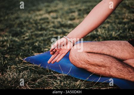 Un giovane attivo pratica yoga in un parco con lo skyline della città sullo sfondo. È ideale per il benessere, il fitness all'aperto e campagne di lifestyle urbano che prevedono yoga e vita sana. Foto Stock
