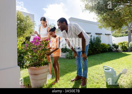 Famiglia che ama il giardinaggio insieme nel cortile, sorridendo e coltivando piante Foto Stock
