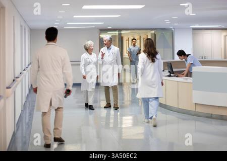Medici cinesi anziani di sesso maschile e femminile che parlano mentre camminano nel corridoio dell'ospedale Foto Stock