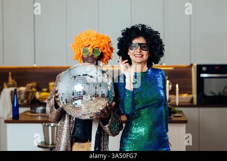 Felice coppia multietnica senior a casa che si gode un momento di festa. Una calda scena di stile di vita che mette in risalto relazioni durature e compagnia nella vita successiva. Adatto a temi di invecchiamento, famiglia e supporto. Foto Stock