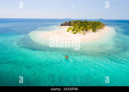 Coppia in kayak su una spiaggia tropicale con acqua blu e palme a Coron, Filippine. Questo scatto di stile di viaggio cattura l'avventura e il romanticismo. Perfetto per turismo, vacanze sull'isola e campagne di vacanza. Foto Stock