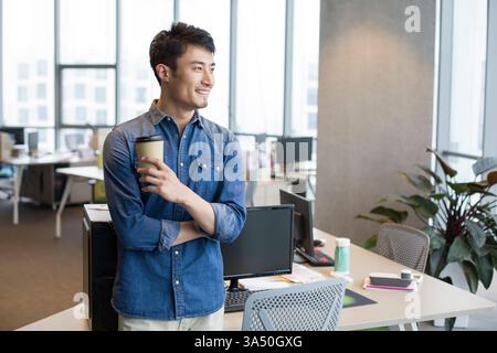 Giovane cinese che fa una pausa caffè in un ufficio. Uno scenario rilassato e contemporaneo adatto a campagne di business, di lavoro e di lifestyle urbano. Foto Stock