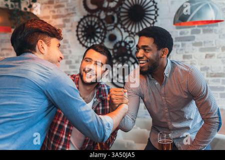 Un gruppo multirazziale di amici condivide un allegro saluto in un vivace pub. Questa variegata scena cattura l'amicizia, socializzazione informale e un'atmosfera rilassata da bar con birra. Foto Stock
