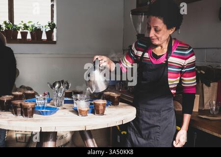 Donna ispanica che versa caffè in bicchieri su un tavolo di legno nella caffetteria Foto Stock