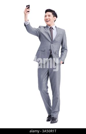 Il giovane uomo d'affari cinese con un vestito posa con un telefono cellulare in un ritratto di studio. Questa immagine aziendale esperta di tecnologia è adatta per la tecnologia, la comunicazione e il branding aziendale, con spazio di testo. Foto Stock