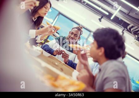 Gruppi diversi di colleghi d'affari che condividono una pausa pranzo a base di pizza in un ambiente di ufficio. La scena schietta mette in evidenza il lavoro di squadra, la collaborazione e una cultura del luogo di lavoro rilassata. Perfetto per le comunicazioni aziendali, la diversità e lo stile di vita dell'ufficio. Foto Stock
